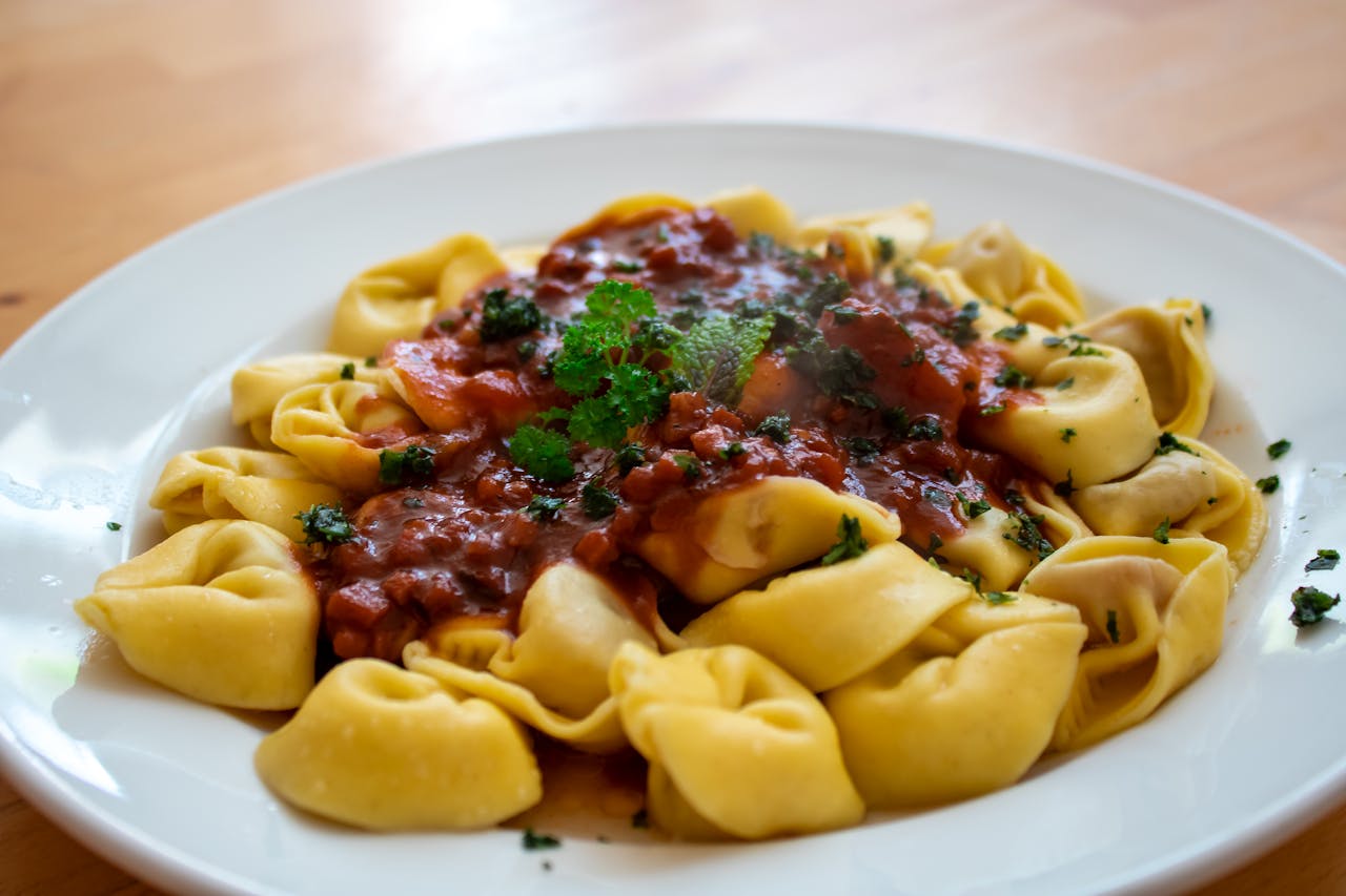 who-we-are Close-up of tortellini with rich tomato basil sauce on a white plate.